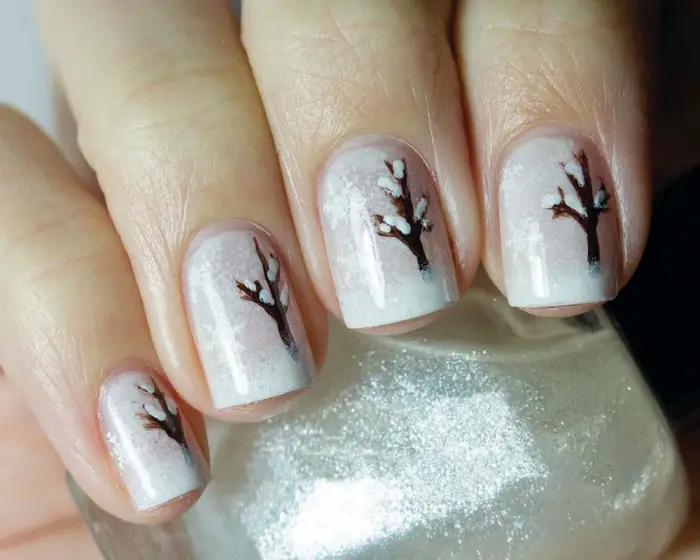 idée pour décoration ongles de Noel avec base blanche à effet enneigé et dessin d&amp;#39;arbre marron